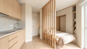 Studio lumineux avec kitchenette moderne, coin nuit séparé par une claustra en bois et rangements intégrés.